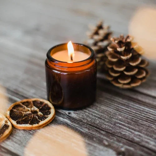 Soy candle in amber jar burning on wood table with dried oranges and pinecones