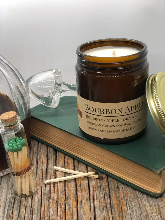 Bourbon apple scented soy wax candle in amber jar with matches on rustic wood table