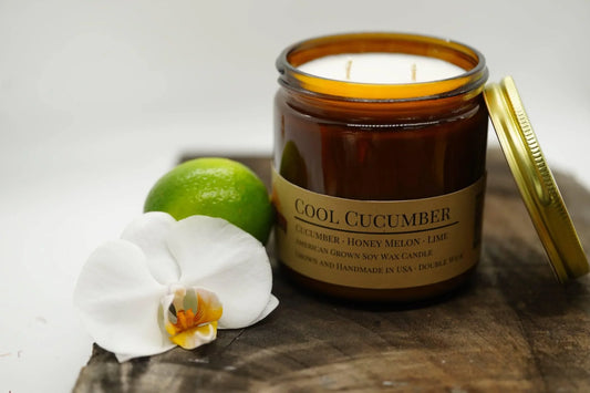 Amber jar soy wax candle labeled Cool Cucumber with lime and white orchid on wooden surface