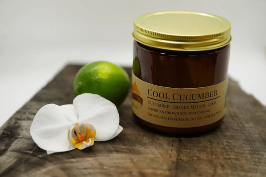 Cool Cucumber soy wax candle in amber jar with gold lid, lime and white orchid on wood surface
