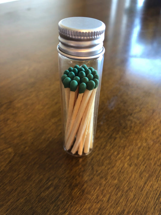 Glass jar of green-tipped wooden matches with metal lid on wooden table