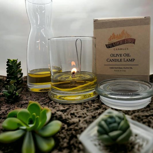 Olive oil candle lamp burning in glass jar with box, surrounded by succulents.