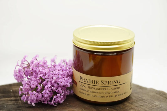 Prairie Spring soy wax candle in amber jar with gold lid beside lilac flowers on wood