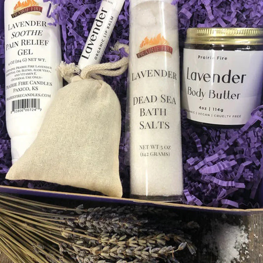 Lavender gift set with pain relief gel, body butter, bath salts, lip balm, and dried lavender on purple paper.