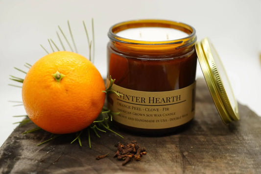 Winter Hearth soy wax candle in amber jar beside orange, rosemary, and cloves on wood