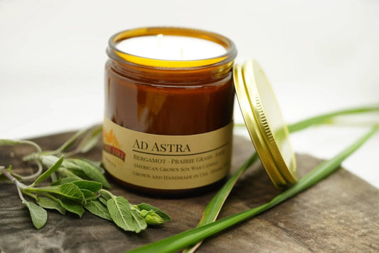 Amber apothecary jar soy wax candle labeled Ad Astra with herbs and gold lid