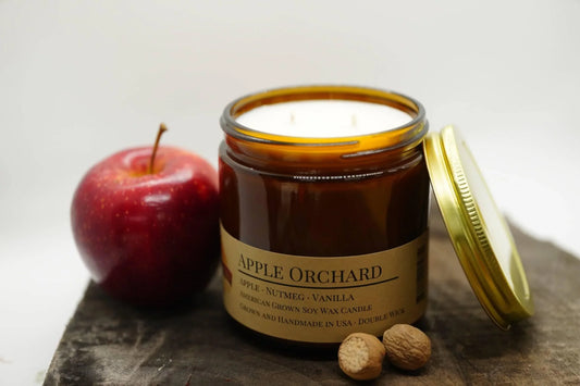 Apple Orchard soy wax candle in amber jar with red apple and nutmeg on rustic wooden surface