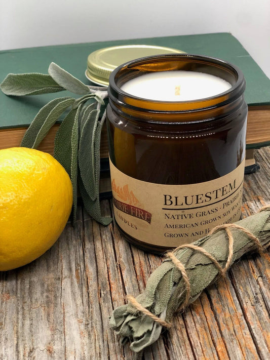 Soy wax candle in amber jar on rustic wood with sage bundle, lemon, and books
