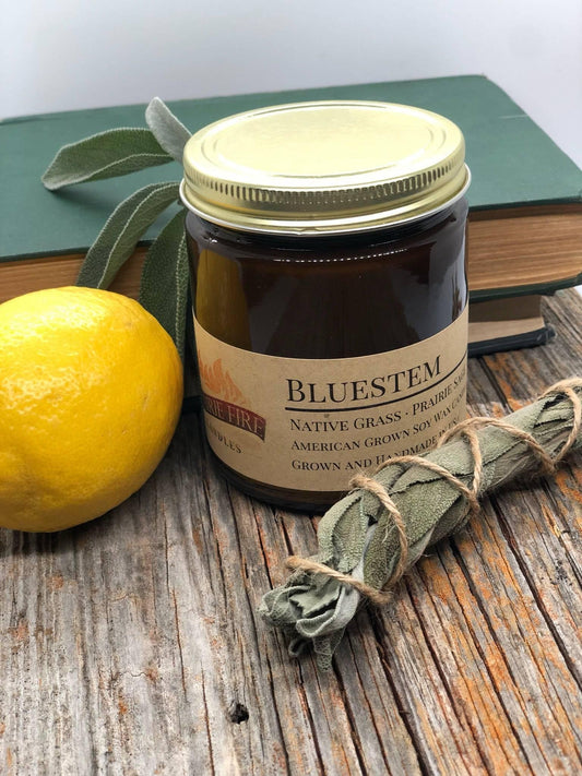 Bluestem soy wax candle in amber jar with lemon, sage bundle, and books on rustic wood