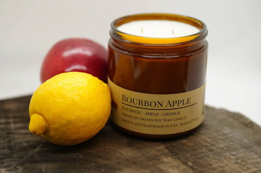 Bourbon apple soy wax candle in amber jar with lemon and red apple on wooden surface