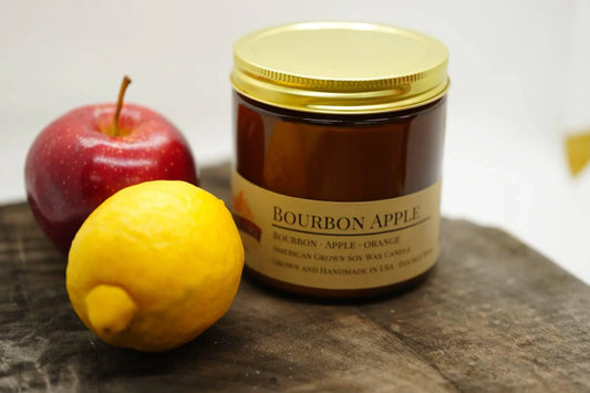 Bourbon apple soy wax candle in amber jar with gold lid, apple and lemon beside it