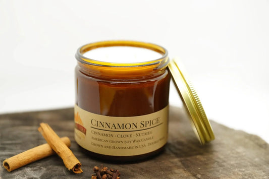 Cinnamon Spice soy wax candle in amber jar with gold lid, cinnamon sticks and cloves beside it