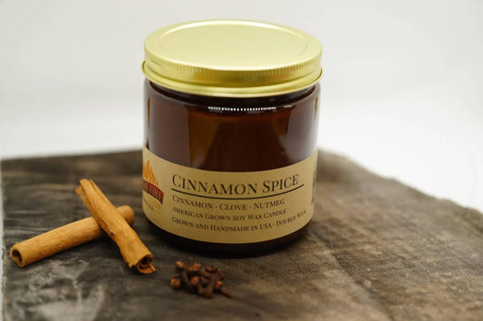 Cinnamon spice soy wax candle in amber jar with gold lid, cinnamon sticks, and cloves