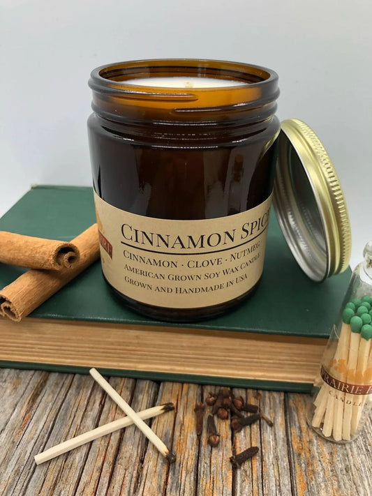 Cinnamon spice soy wax candle in amber jar with lid, cinnamon sticks, cloves, matches on wood