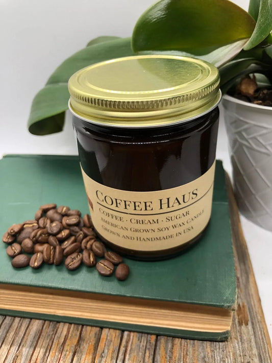 Coffee Haus soy wax candle in amber jar with gold lid, coffee beans, and green book