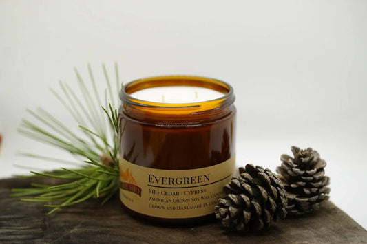 Evergreen soy wax candle in amber jar with pine needles and pine cones, double wick