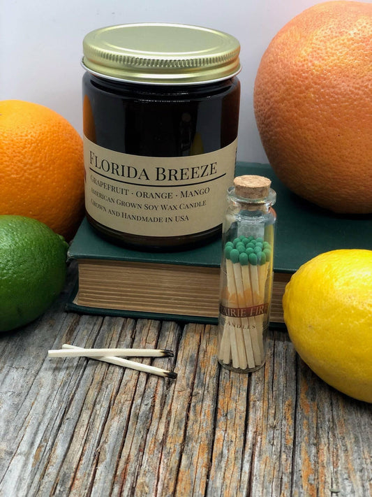 Florida Breeze soy wax candle in amber jar with citrus fruits, book, jar of matches, and burnt matches