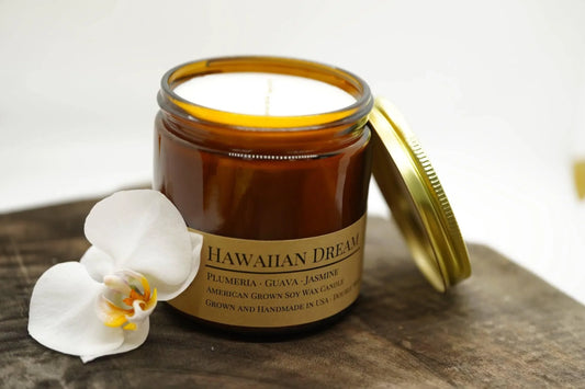 Amber jar Hawaiian Dream soy wax candle with gold lid and white orchid on wood surface