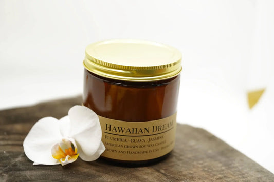 Hawaiian Dream soy wax candle in amber jar with gold lid, white orchid beside it on wood