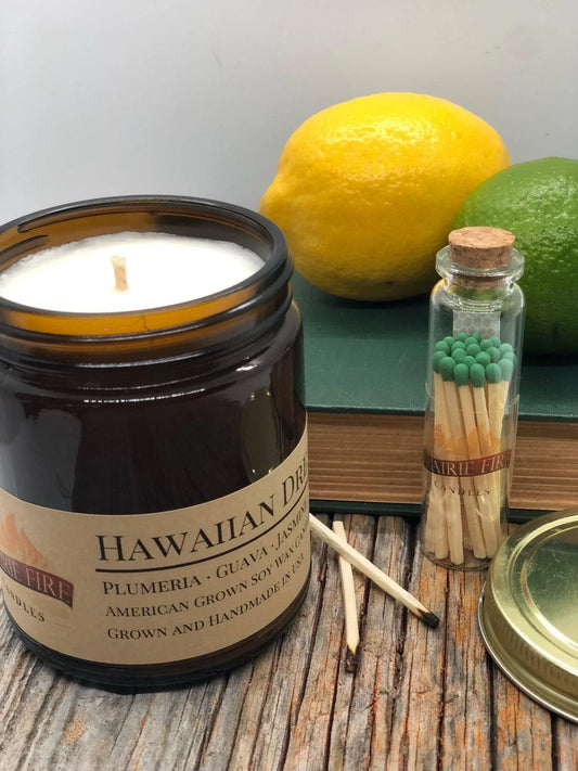Hawaiian Dream soy wax candle in amber jar with matches, lemon, and lime on rustic wood table.