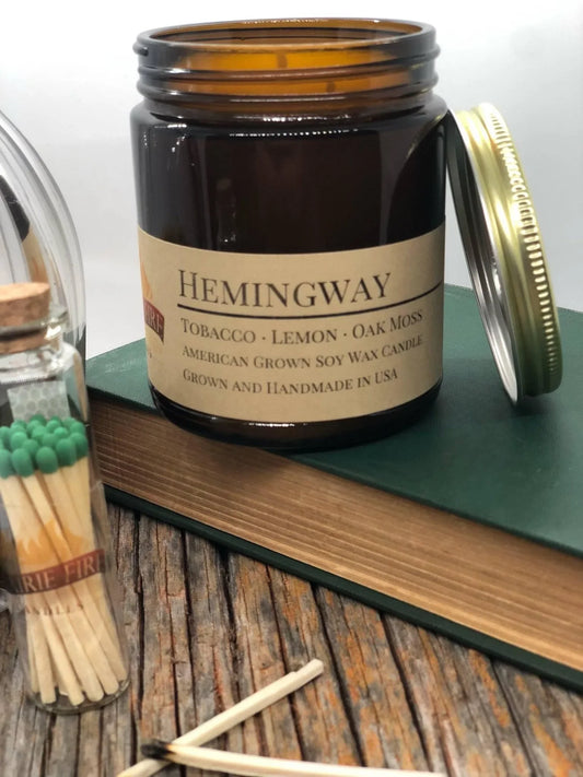 Soy wax candle in amber apothecary jar with Hemingway label, matches and books nearby