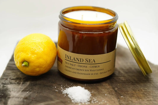Amber jar soy wax candle labeled Inland Sea with lemon and sea salt on rustic wood