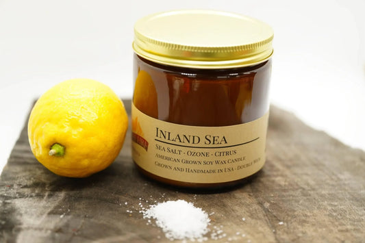 Amber jar soy wax candle labeled Inland Sea with lemon and sea salt on wooden surface