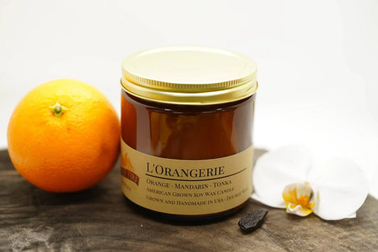 L'Orangerie soy wax candle in amber jar with orange, tonka bean, and white orchid on wood
