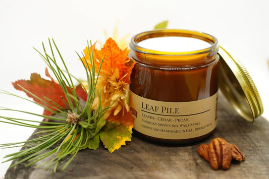 Leaf Pile soy wax candle in amber jar with fall leaves, pine needles, and pecans decor.
