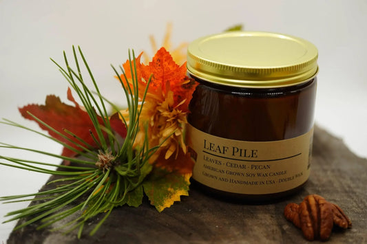 Leaf Pile soy wax candle in amber jar with gold lid, surrounded by autumn leaves, pine, and pecan