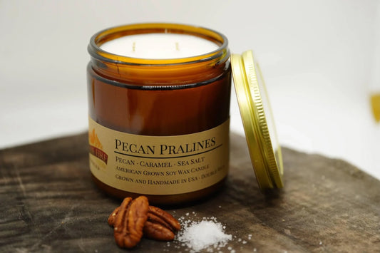 Pecan Pralines soy wax candle in amber jar with gold lid, pecans and sea salt on wood