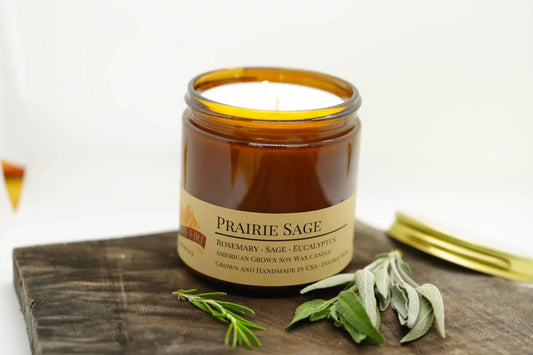 Prairie Sage soy wax candle in amber jar with herbs, wood lid, and rustic background