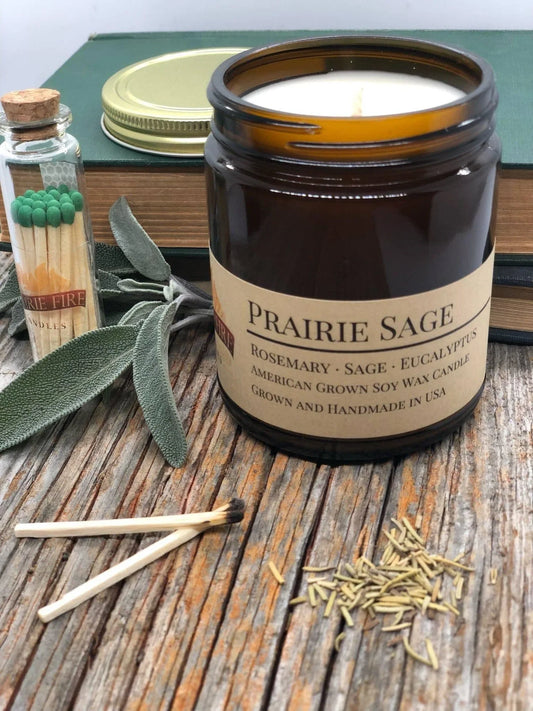 Prairie Sage soy wax candle in amber jar with sage leaves, matches, and dried herbs on wood surface