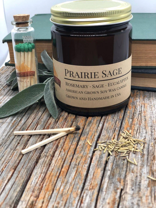 Prairie Sage soy wax candle in amber jar with matches, sage leaves, and herbs on rustic wood.