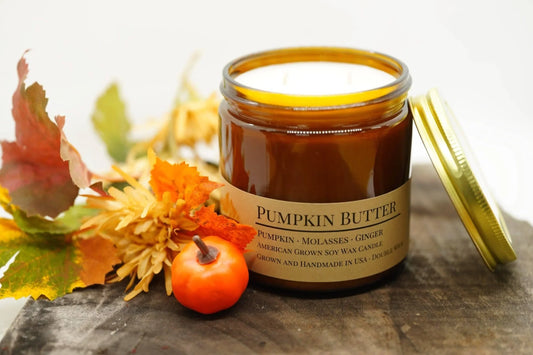 Pumpkin Butter soy wax candle in amber jar with lid, autumn leaves, and mini pumpkin decor.