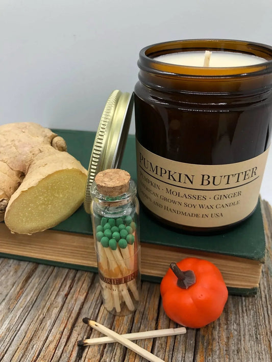 Pumpkin Butter soy wax candle in amber jar with ginger root, book, glass jar of matches, and mini pumpkin