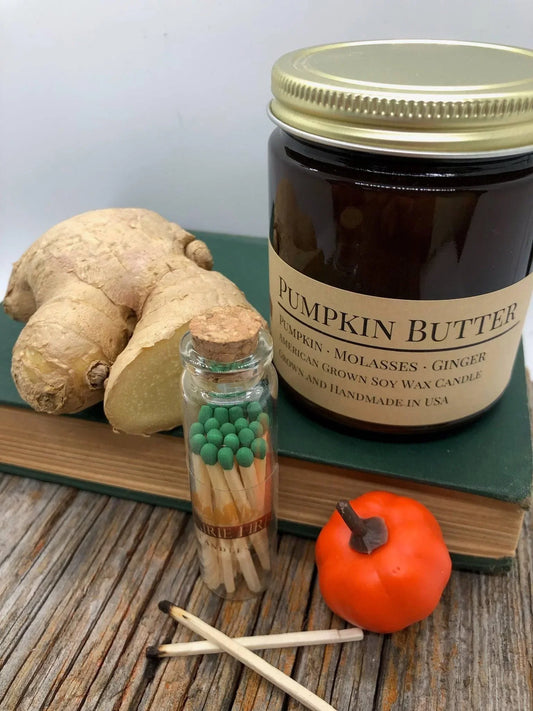 Pumpkin Butter soy wax candle with ginger root, matches, and a small pumpkin on wood table.