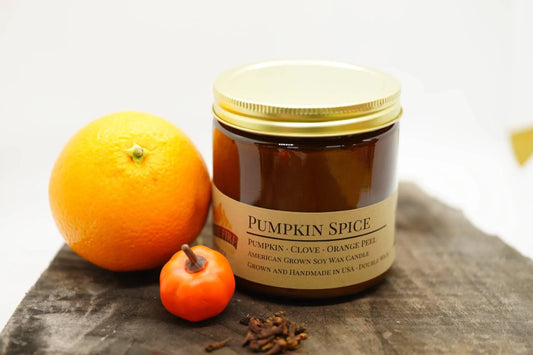 Pumpkin spice soy wax candle jar with orange, chili pepper, and whole cloves on rustic wood