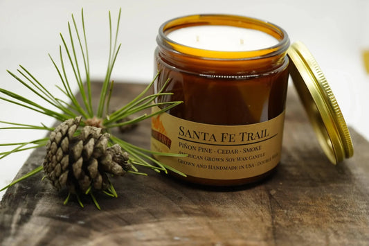 Santa Fe Trail soy wax candle in amber jar with gold lid, pine cone and needles on wood
