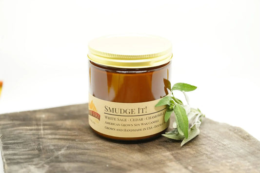 Amber apothecary jar soy wax candle labeled Smudge It! with sage leaves on rustic wood