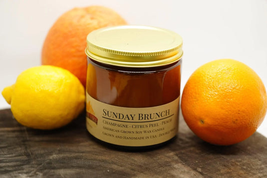 Sunday Brunch soy wax candle in amber jar with lemon, orange, and grapefruit on wood surface