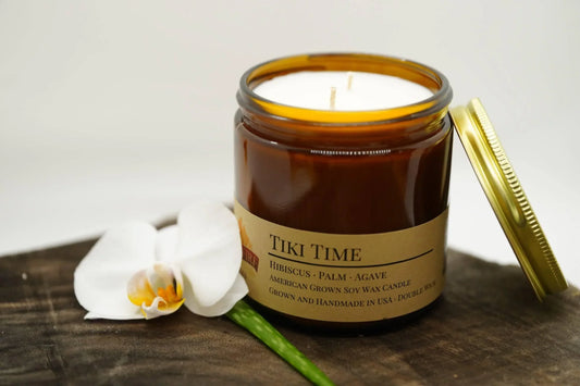 Amber jar Tiki Time soy wax candle with gold lid and white orchid on wooden surface
