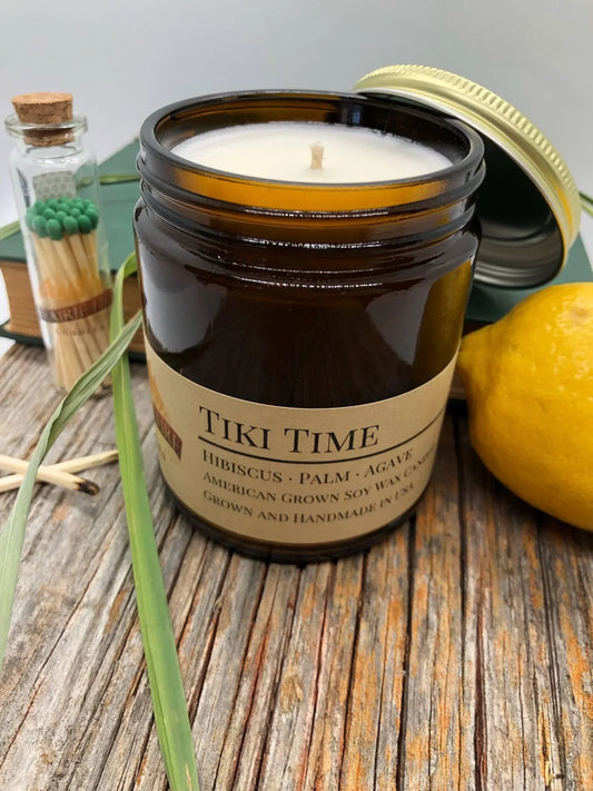 Tiki Time soy wax candle in amber jar with matches, lemon, and grass on rustic wood
