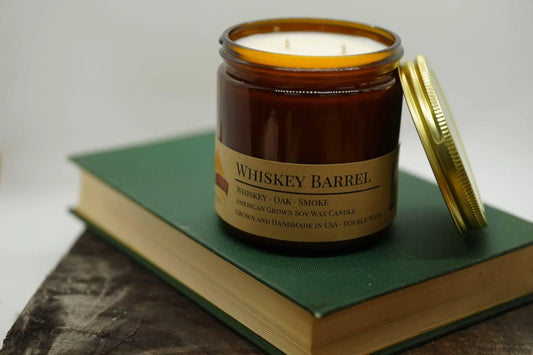 Whiskey Barrel soy wax candle in amber jar with gold lid on green book