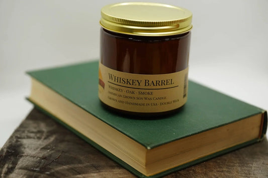 Whiskey Barrel soy wax candle in amber jar with gold lid on green book