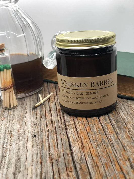 Whiskey Barrel soy wax candle in amber jar on rustic wood with matches and glass decanter
