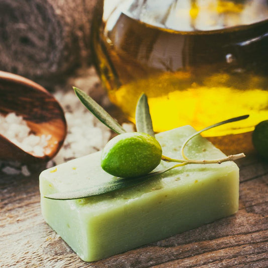 Castile olive oil soap bar with fresh olive and leaves beside a glass jar of olive oil