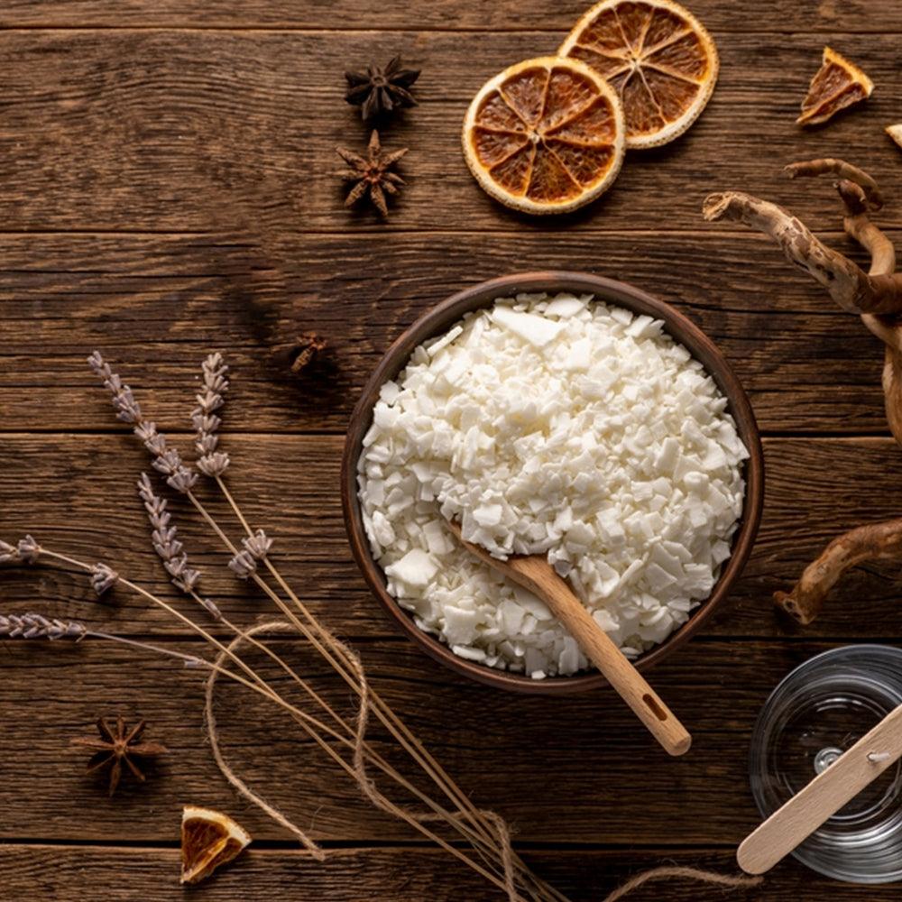 Organic soy wax flakes in a bowl with dried lavender, star anise, and orange slices on wood
