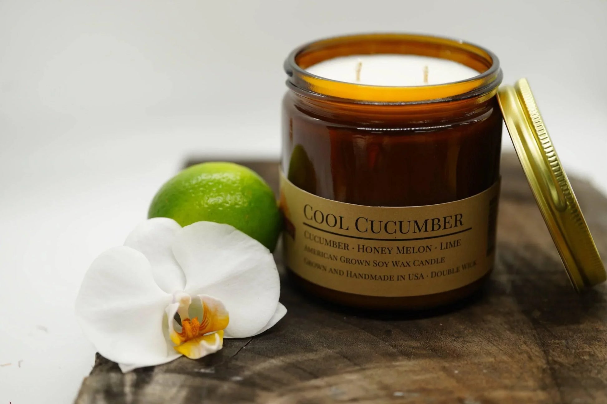Amber jar soy wax candle labeled Cool Cucumber with lime and white orchid on wooden surface