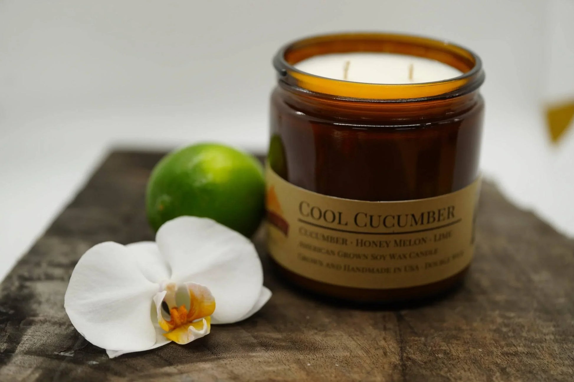 Cool Cucumber soy wax candle in amber jar with a lime and white orchid on rustic wood
